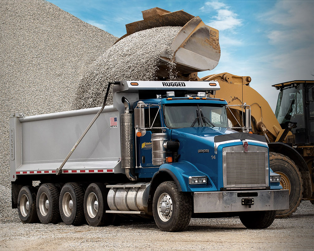 Rugged dump body on a Kenworth chassis being loaded at a gravel site