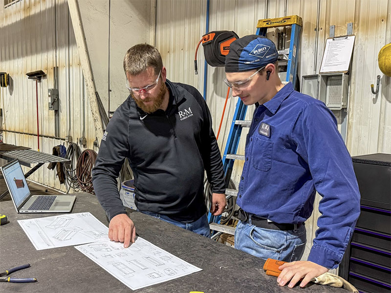 Two men at a table reviewing engineering drawings for a dump body build